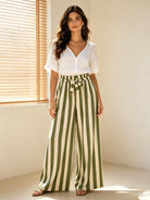 Woman wearing a white blouse and green and white striped pants in a bright room.