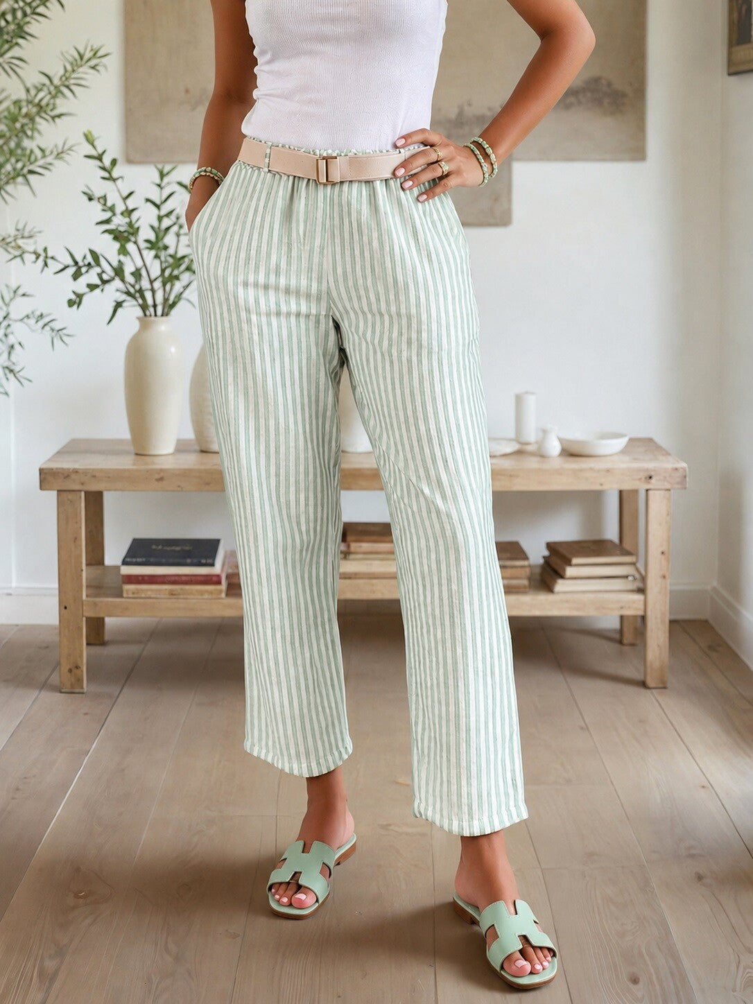 Person wearing light green striped pants and white top in a room with wooden furniture and plants.
