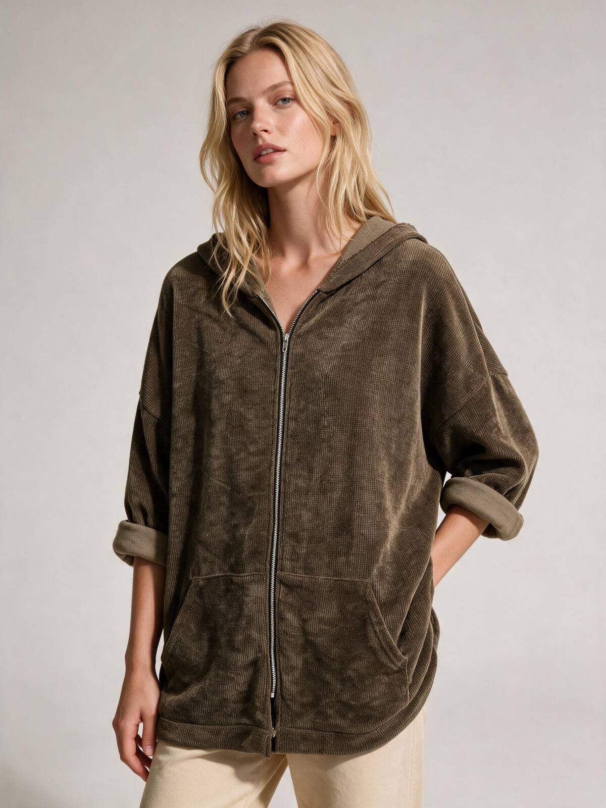 A woman wearing an oversized zip-up hooded sweatshirt in a dark brown textured fabric, paired with light beige pants