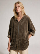 A woman wearing an oversized zip-up hooded sweatshirt in a dark brown textured fabric, paired with light beige pants