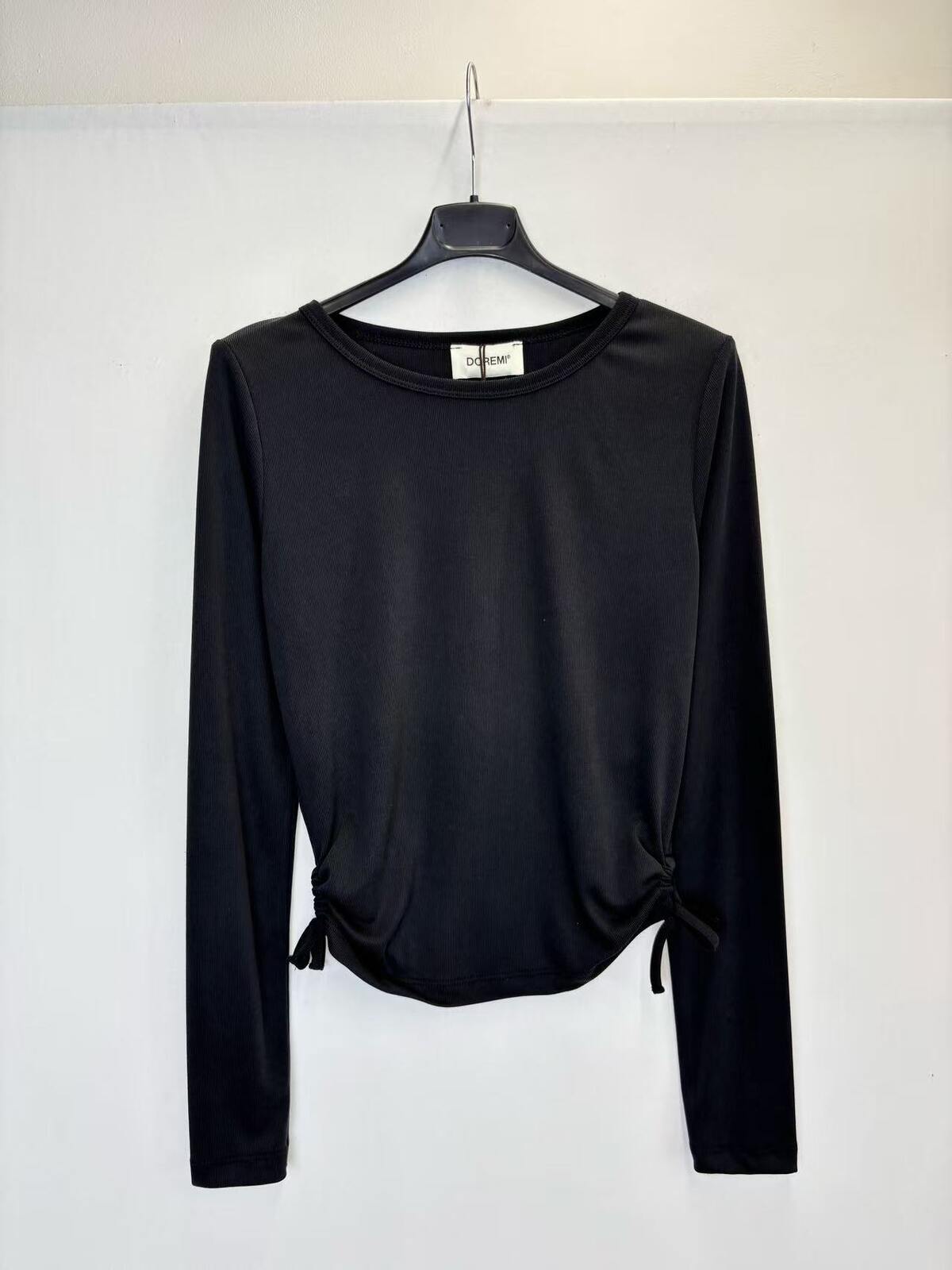A black long-sleeve crop top with side tie details, hanging on a black hanger against a plain white wall.