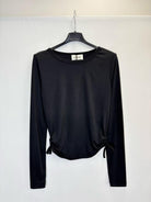 A black long-sleeve crop top with side tie details, hanging on a black hanger against a plain white wall.