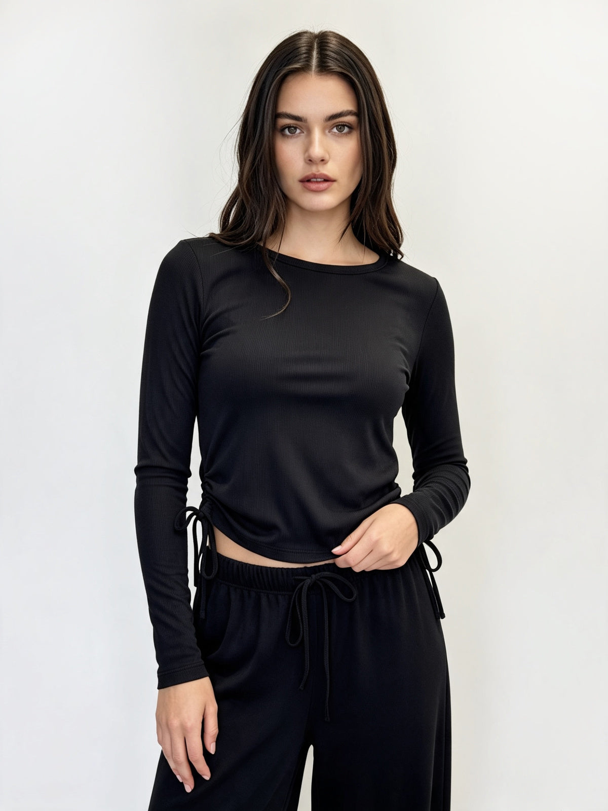 A woman modeling a black long-sleeve crewneck top with side drawstrings, paired with black drawstring pants