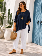 Woman in navy top and white pants standing outdoors with plants and a blue door in the background