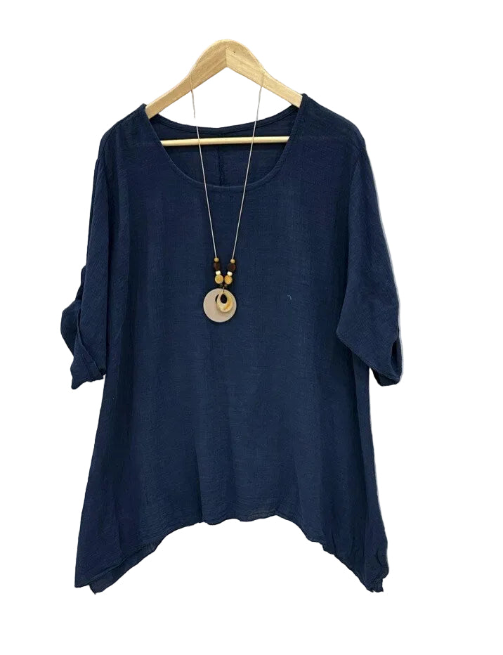 Navy blue top on a hanger with a necklace against a textured white background