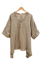 Taupe blouse with ruffled details on a hanger against a white background