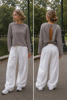 A woman modeling a taupe long-sleeve crop top with a back cutout and white wide-leg pants in an outdoor park setting, shown in front and back views.