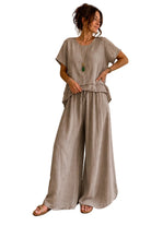 A woman models a two-piece linen set consisting of a short-sleeve top and wide-leg trousers in a light taupe-beige color