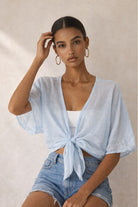 Woman wearing a light blue tied top and denim shorts against a neutral background