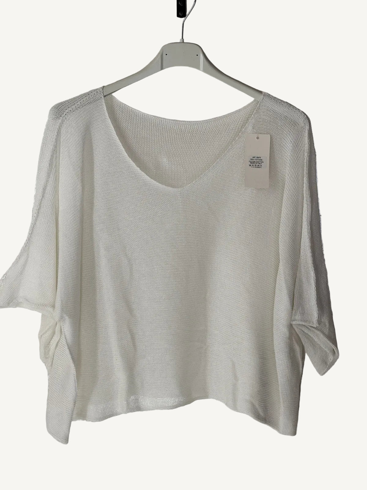 White sweater on a hanger with a visible tag against a textured white background