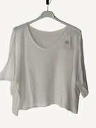 White sweater on a hanger with a visible tag against a textured white background