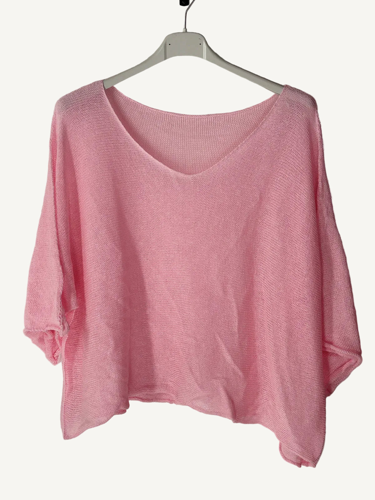 Pink sweater on a hanger against a textured wall.
