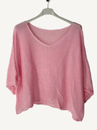 Pink sweater on a hanger against a textured wall.