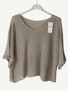 Brown sweater on a hanger with a tag against a textured wall.