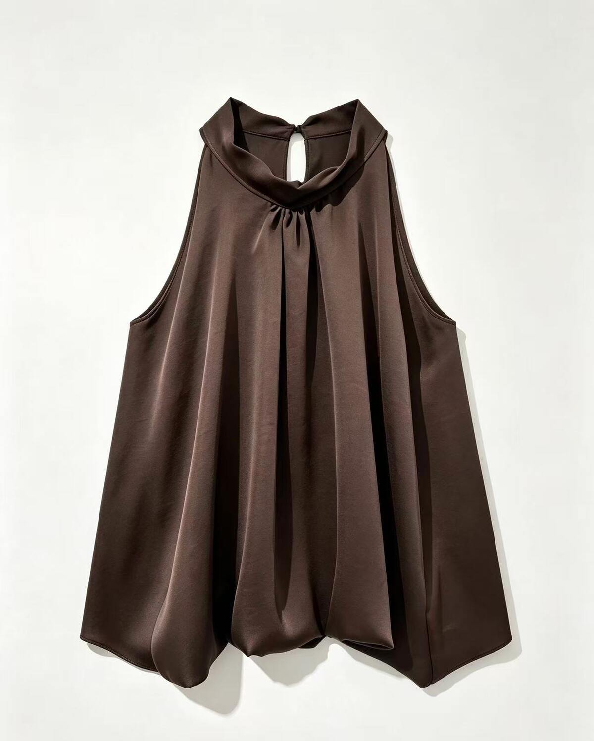A sleeveless dark brown top with a draped, high-neck collar and a gathered front, displayed against a plain off-white background.