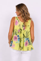 Woman wearing a yellow floral sleeveless top against a white background