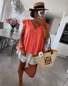 A woman wearing a coral sleeveless top, white ruffled shorts, a straw hat, and carrying a beige woven tote bag 