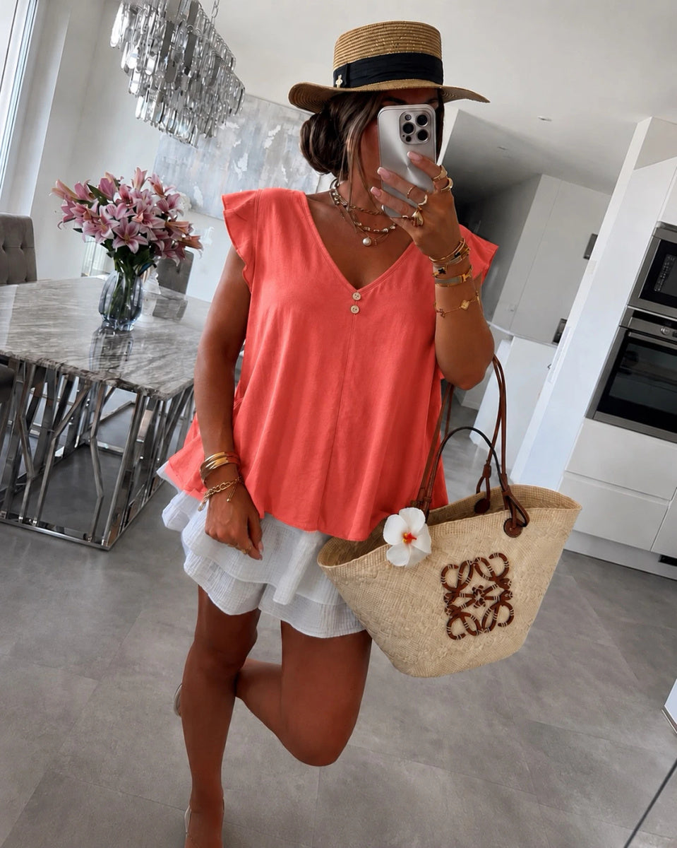 A woman wearing a coral sleeveless top, white ruffled shorts, a straw hat, and carrying a beige woven tote bag 