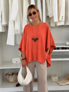 A woman wearing a loose, short-sleeved orange top and beige pants stands in front of a white closet filled with white clothing. 