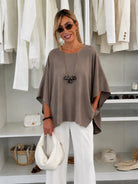 A woman wearing a taupe-brown short-sleeve bubble-neck top and white wide-leg pants
