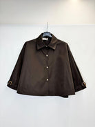 A dark brown trench style jacket with a pointed collar and front buttons, hanging on a black hanger against a plain white wall.