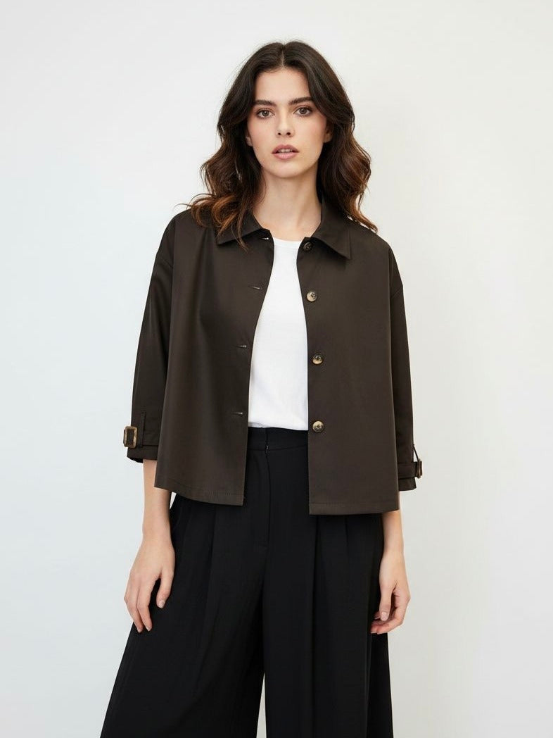 A woman modeling a dark brown cropped button-up jacket with three-quarter sleeves, worn over a white top and wide-leg trousers