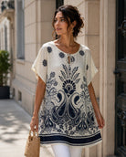 A woman wearing a short-sleeve tunic top with a navy blue floral and paisley print, standing on a city sidewalk next to a beige stone building.
