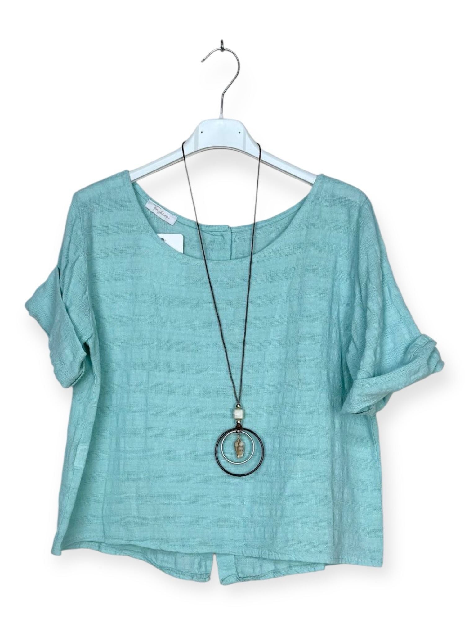 A light aqua blue short-sleeve top with a relaxed fit, hanging on a white hanger with a long black pendant necklace draped over it, against a plain white background.