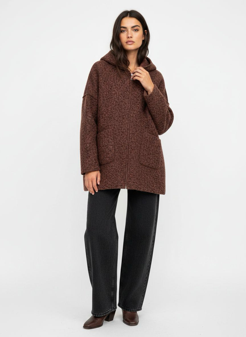 A woman modeling a brown textured hooded jacket with black wide-leg jeans and brown boots