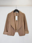 A tan textured bouclé open-front jacket with wide lapels and rolled cuffs, hanging on a black hanger 