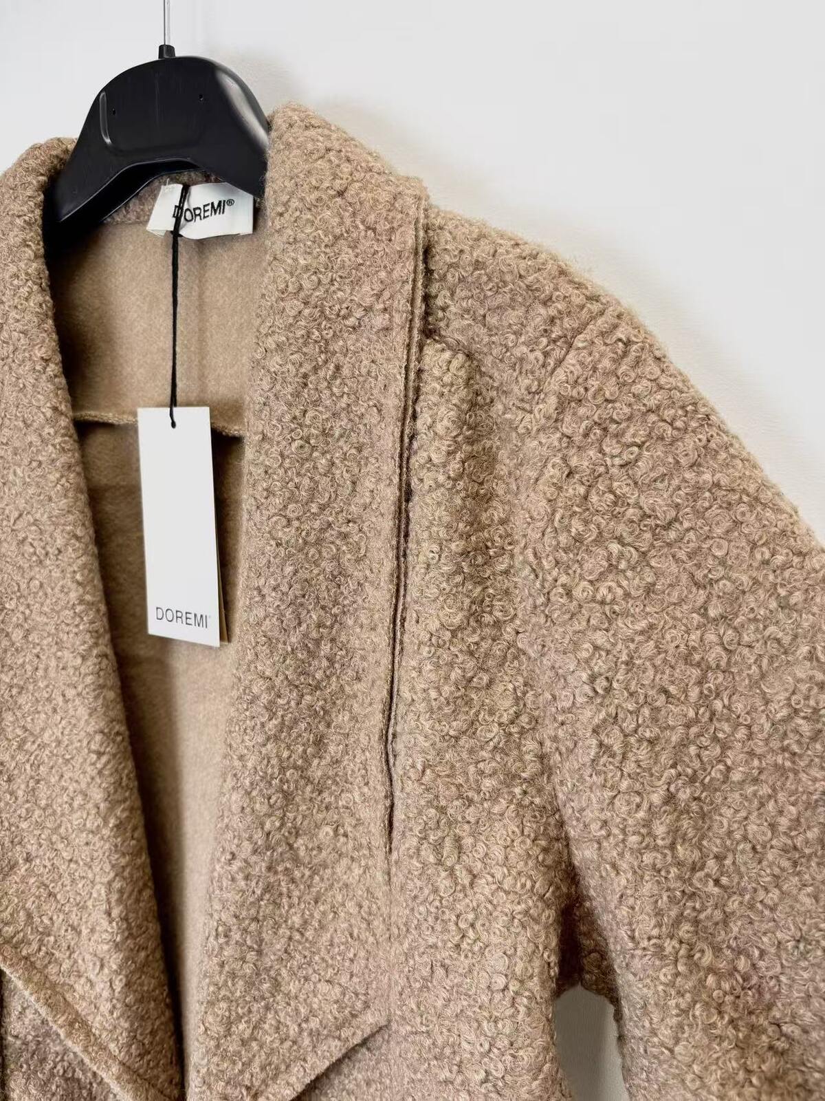 A close-up of textured bouclé coat in a warm camel beige color, hanging on a black hanger 
