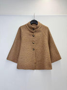 A brown textured bouclé jacket with a mock neck and three-quarter sleeves, hanging on a black hanger against a plain white wall.