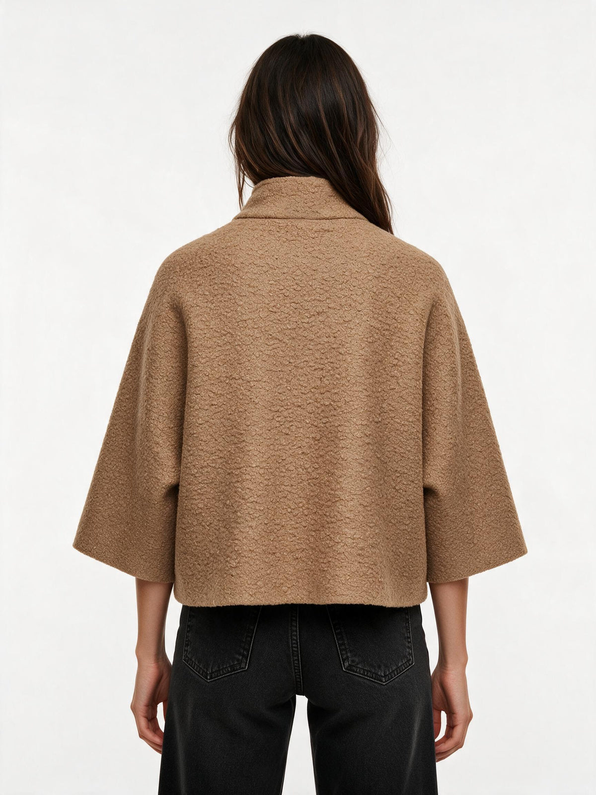 A model viewed from the back wearing a cropped, wide-sleeved camel-colored textured jacket and black jeans against a plain white background.