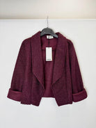 A textured, open-front cropped jacket in a deep plum purple color, hanging on a black hanger 