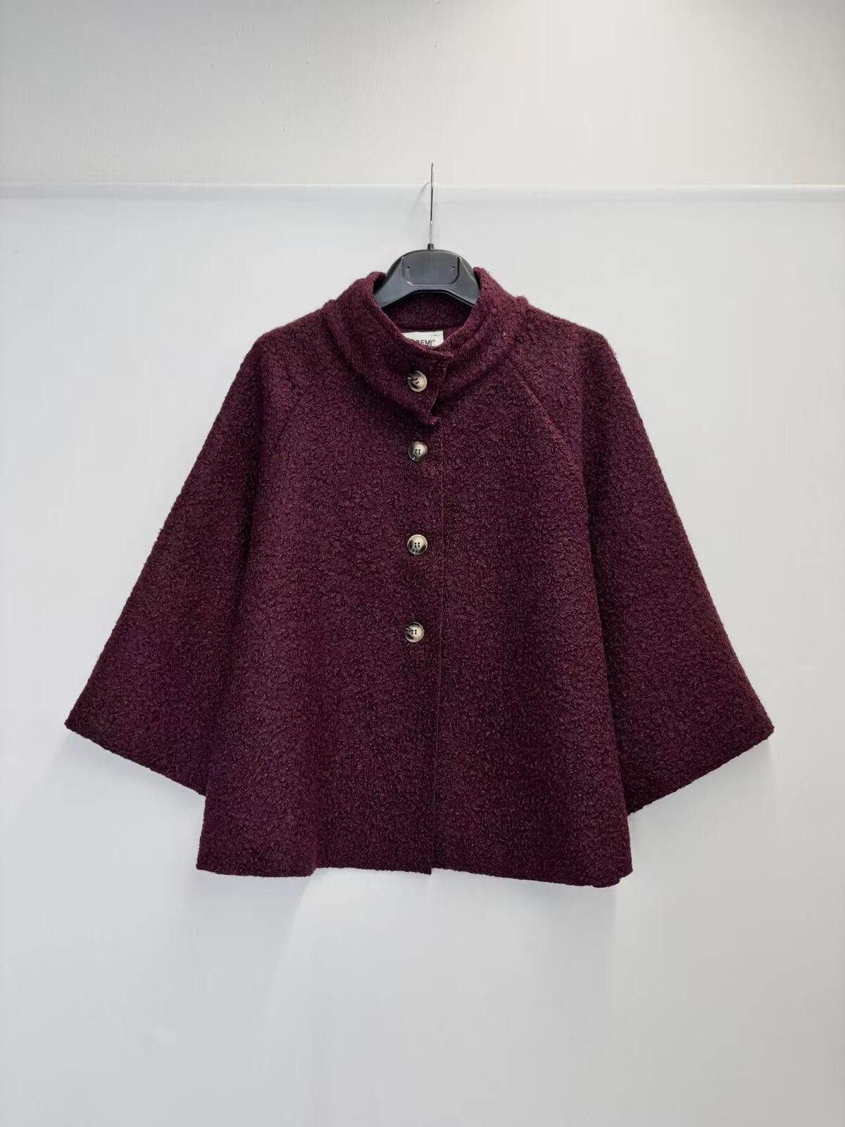 A dark burgundy textured jacket with a mock neck and three silver buttons, hanging on a black hanger against a plain white wall.