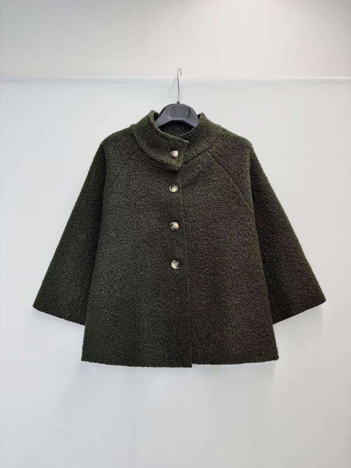 A dark olive green textured jacket with a mock neck and three front buttons, hanging on a black hanger against a plain white wall.