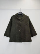 A dark olive green textured jacket with a mock neck and three front buttons, hanging on a black hanger against a plain white wall.