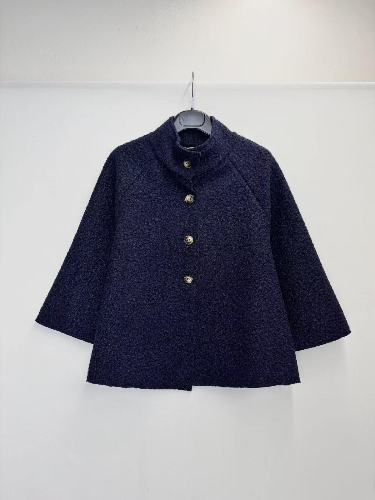 A dark navy blue textured jacket with a high mock neck and gold buttons, hanging on a black hanger against a plain white wall.