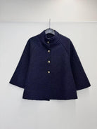 A dark navy blue textured jacket with a high mock neck and gold buttons, hanging on a black hanger against a plain white wall.