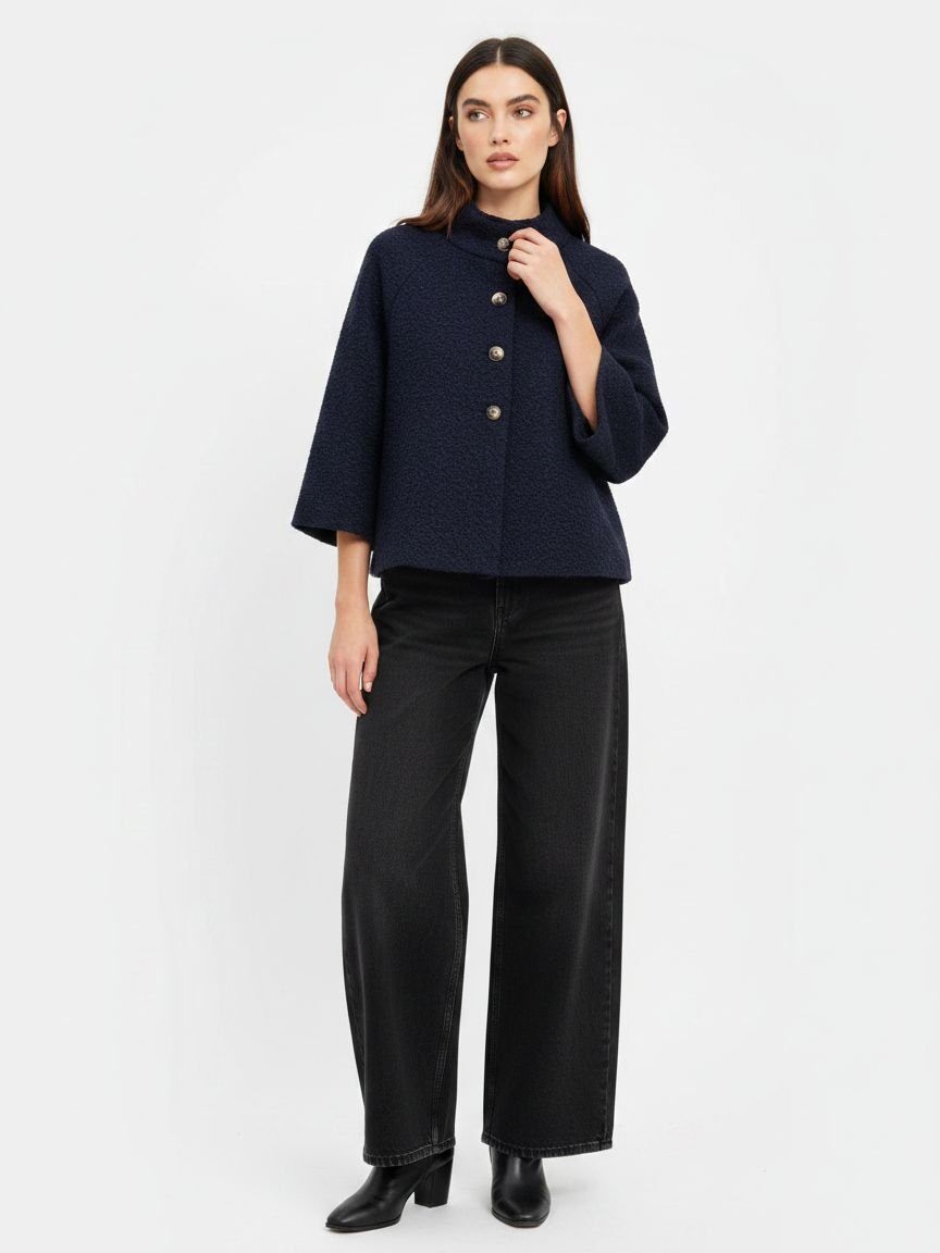 A model wearing a dark navy blue cropped jacket with three-quarter sleeves and gold buttons, paired with black wide-leg trousers and black boots, against a plain white studio background.