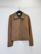 A brown zip-up jacket with a collar and two front patch pockets, hanging on a black hanger against a plain white wall.