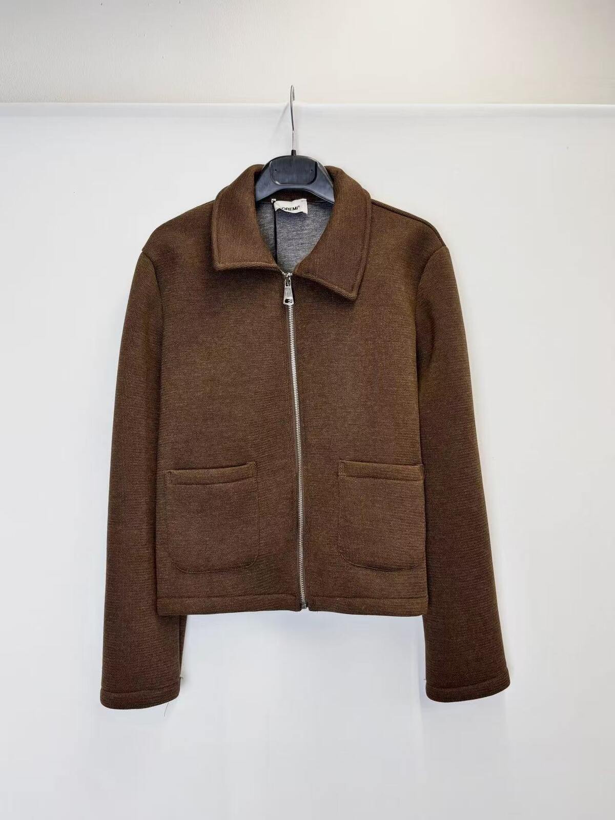 A brown zip-up jacket with a collar and two front patch pockets, hanging on a black hanger against a plain white wall.