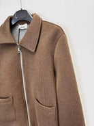 A brown ribbed knit zip-up jacket with a collar and front pockets, hanging on a black hanger against a plain white wall.