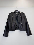 A black cropped faux-leather jacket with silver-tone double-breasted buttons and shoulder epaulets, hanging on a black hanger against a plain white wall.