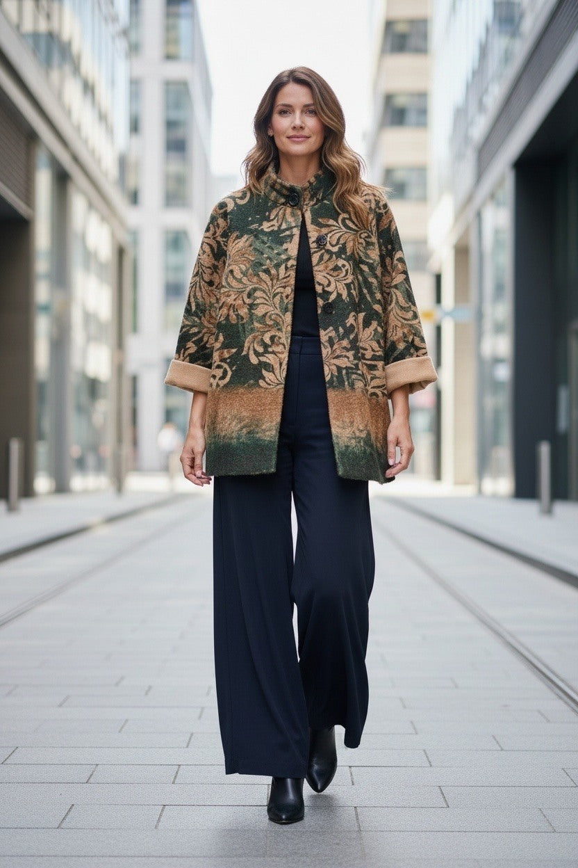 A woman walking down a city street wearing a dark green and brown floral patterned jacket over a black top and wide-leg navy trousers.