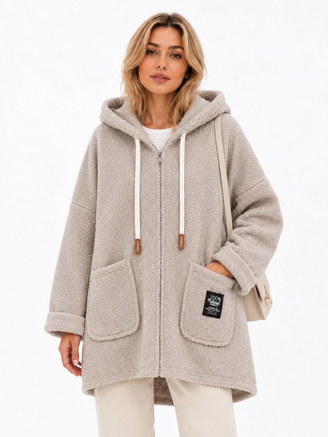 A woman wearing a light beige hooded zip-up coat with white drawstrings and large front patch pockets, photographed against a clean white studio background.