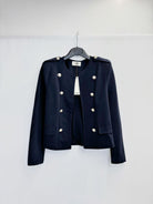 A dark navy blue cropped military-style jacket with silver-tone buttons, hanging on a black hanger against a plain white wall.