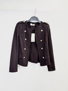 A dark brown cropped military-style jacket with silver buttons, hanging on a black hanger against a plain white wall.