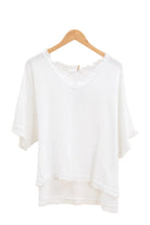 White top on a wooden hanger against a white wall.