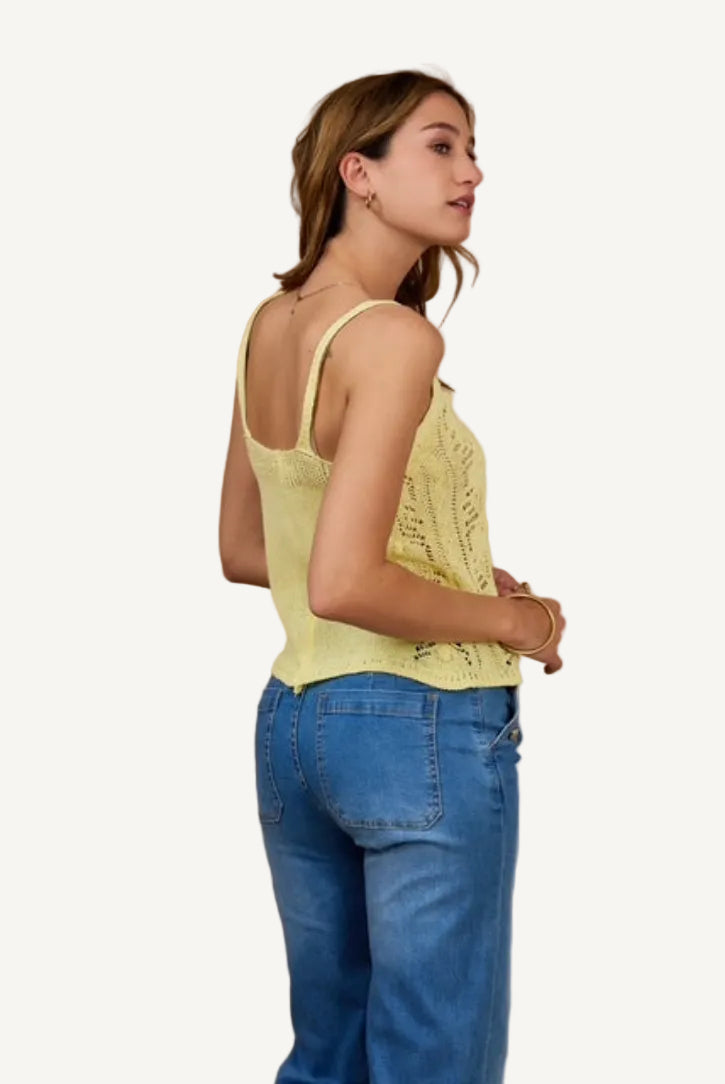 Woman wearing a yellow lace top and blue jeans against a beige background